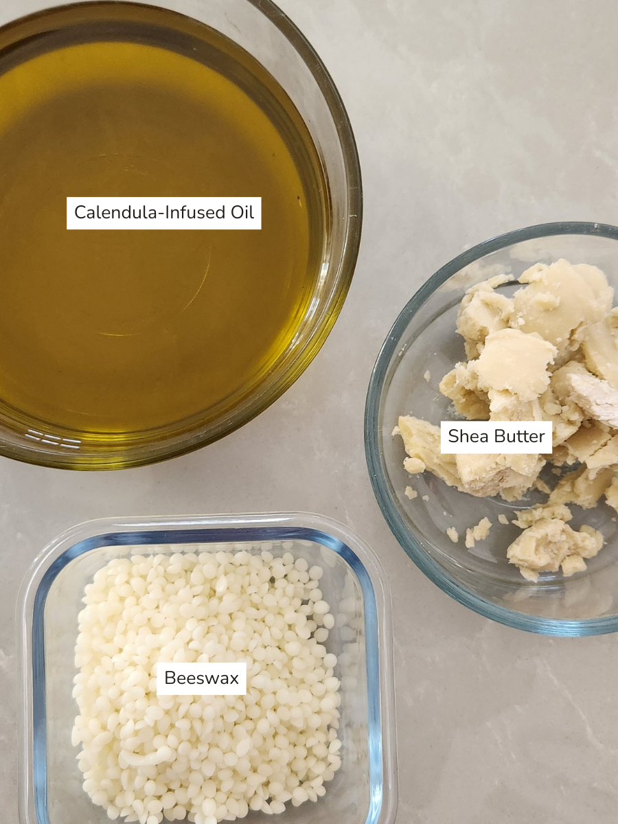 Ingredients for calendula salve recipe — calendula-infused oil, shea butter, and beeswax laid out in glass bowls on a light countertop.