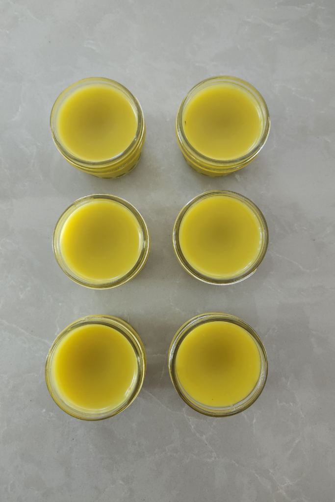 Rows of freshly made calendula salve cooling in glass jars on a light countertop — a simple, natural remedy for dry or irritated skin.