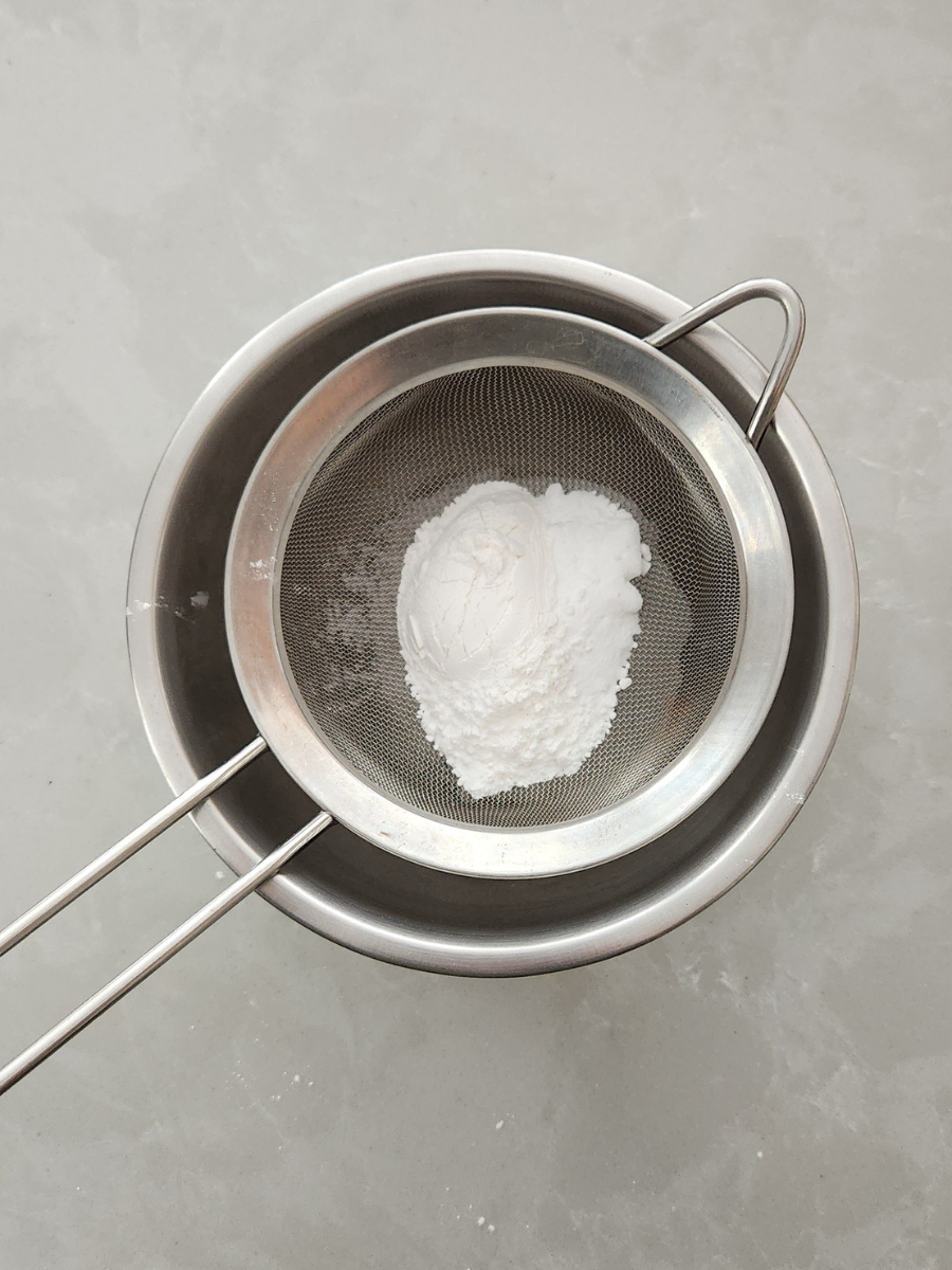 ingredients to make baking powder in a fine mesh strainer over a bowl
