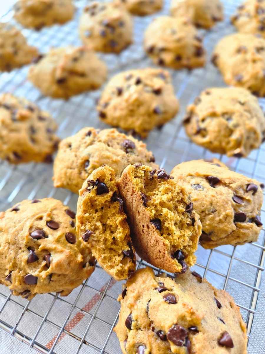 Fresh milled flour pumpkin spice chocolate chip cookies on a cooling rack, with one cookie broken open to show the soft, fluffy center and chocolate chips.