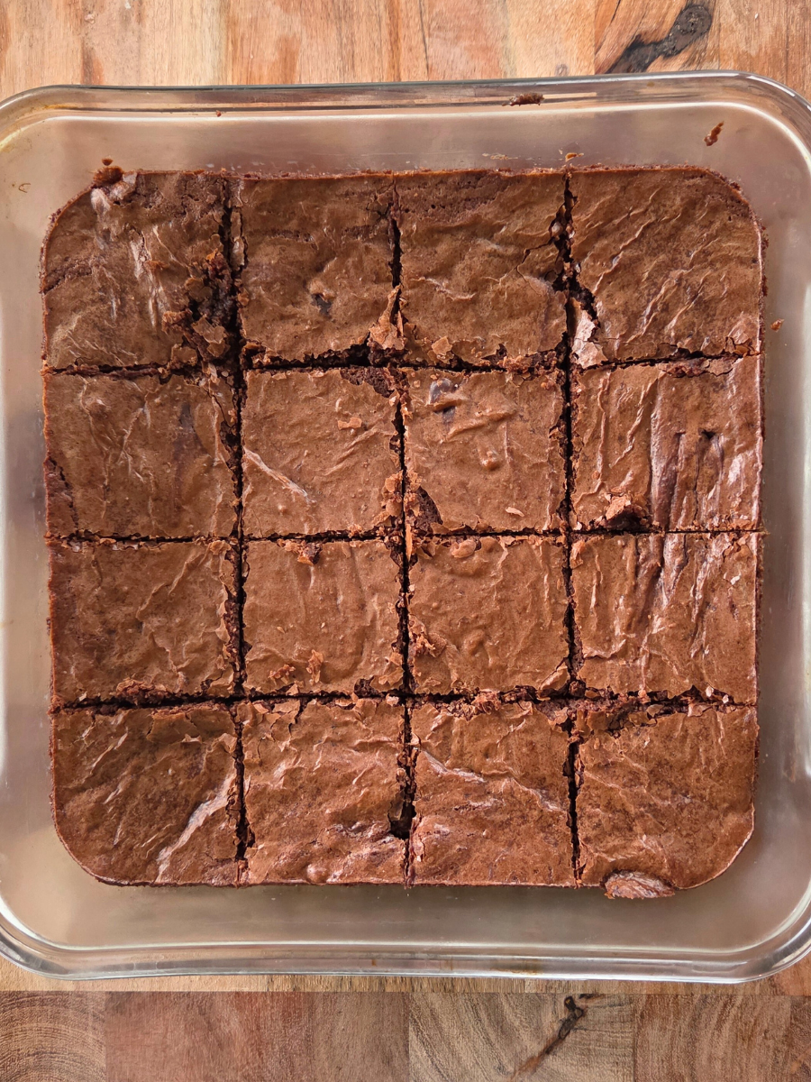 A full pan of fresh milled flour brownies cut into even squares inside a glass baking dish on a wooden surface.
