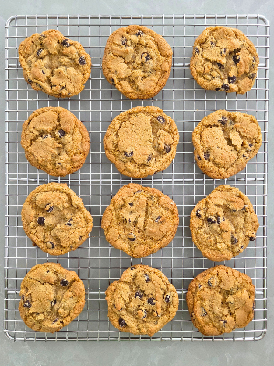 Fresh milled chocolate chip cookies cooling on a metal rack, showing golden crisp edges and tender centers.