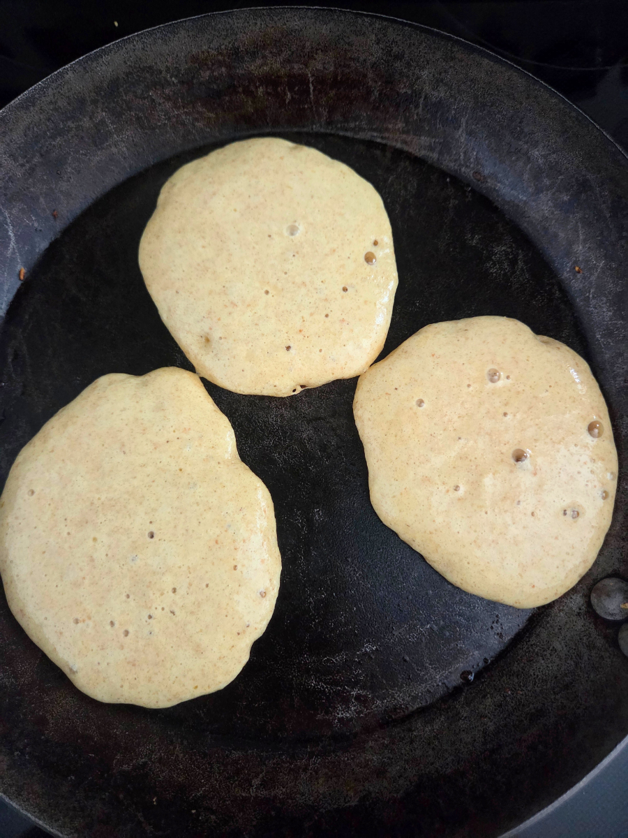 Fresh-milled flour pancake batter cooking on a hot skillet, with bubbles forming across the surface.