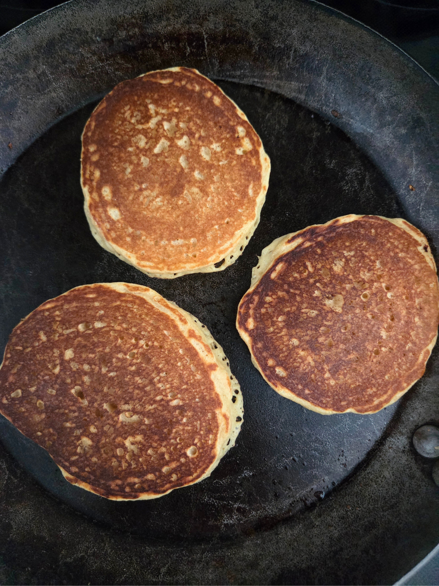 Fresh milled flour pancakes cooking on a skillet, with golden brown tops after flipping.