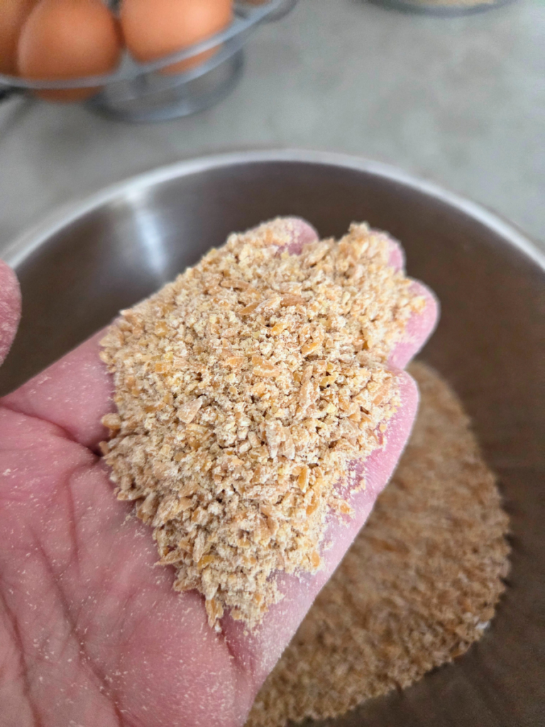 Close-up of coarsely ground einkorn in a hand, showing cracked grains and gritty texture.