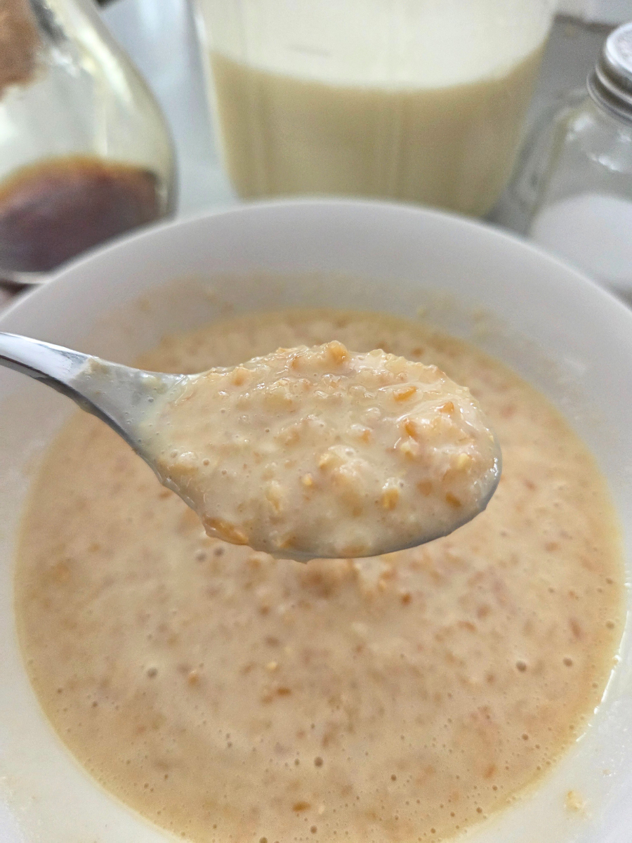 Spoonful of cooked einkorn cream of wheat held over the bowl, showing thick creamy texture and visible grain pieces.