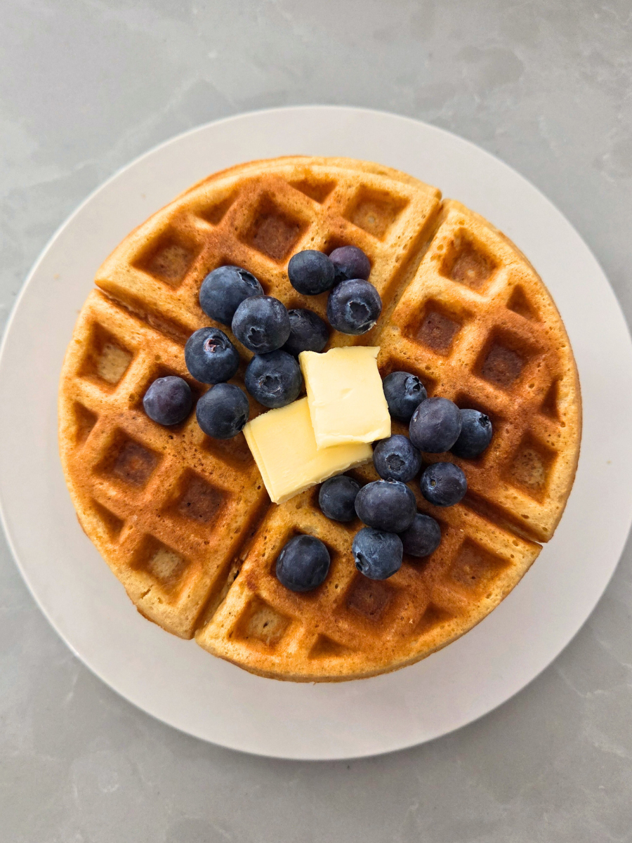 Fresh milled flour waffle topped with butter and blueberries on a white plate