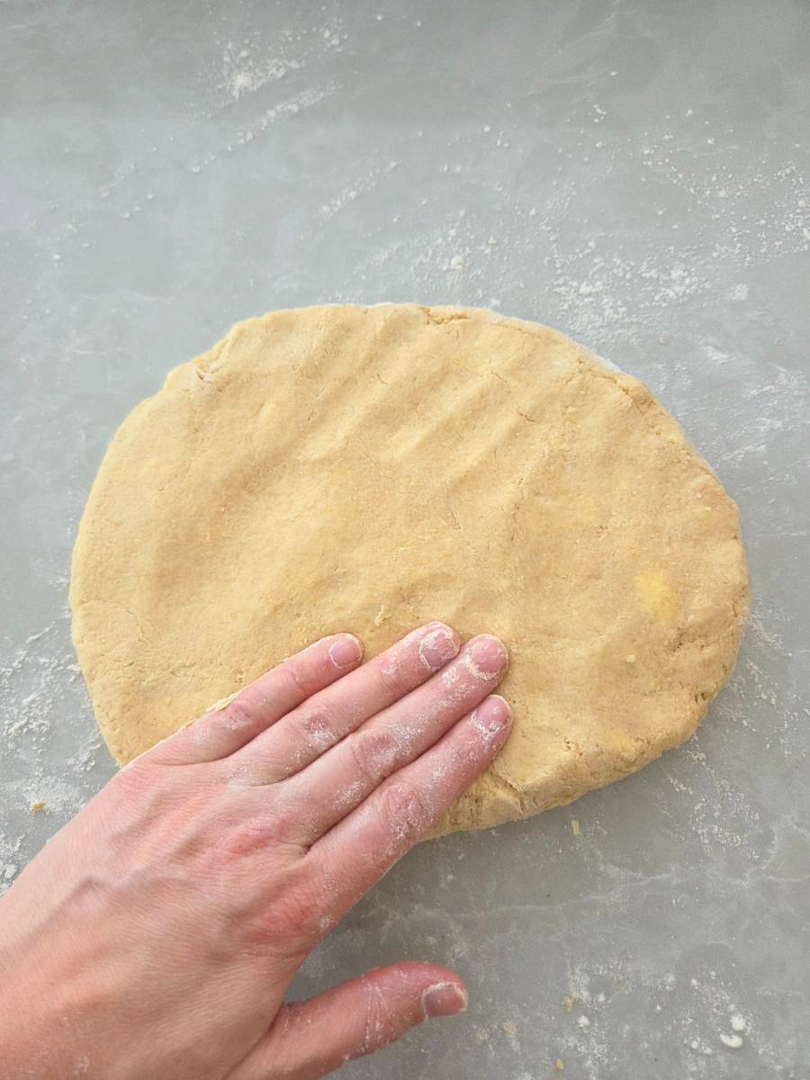 Hands gently pressing biscuit dough flat without using a rolling pin