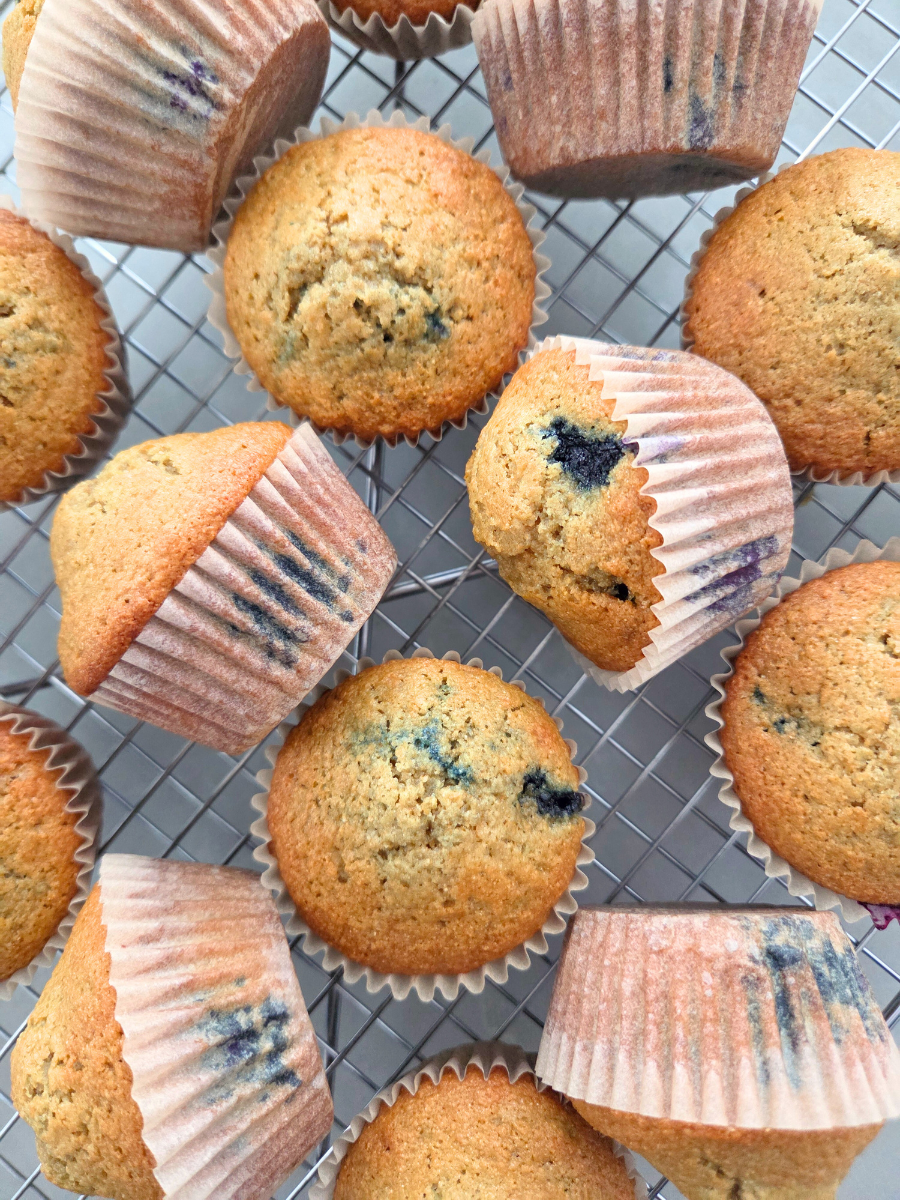 Fresh milled flour blueberry muffins cooling on a wire rack, baked until golden brown with visible blueberries in paper liners.