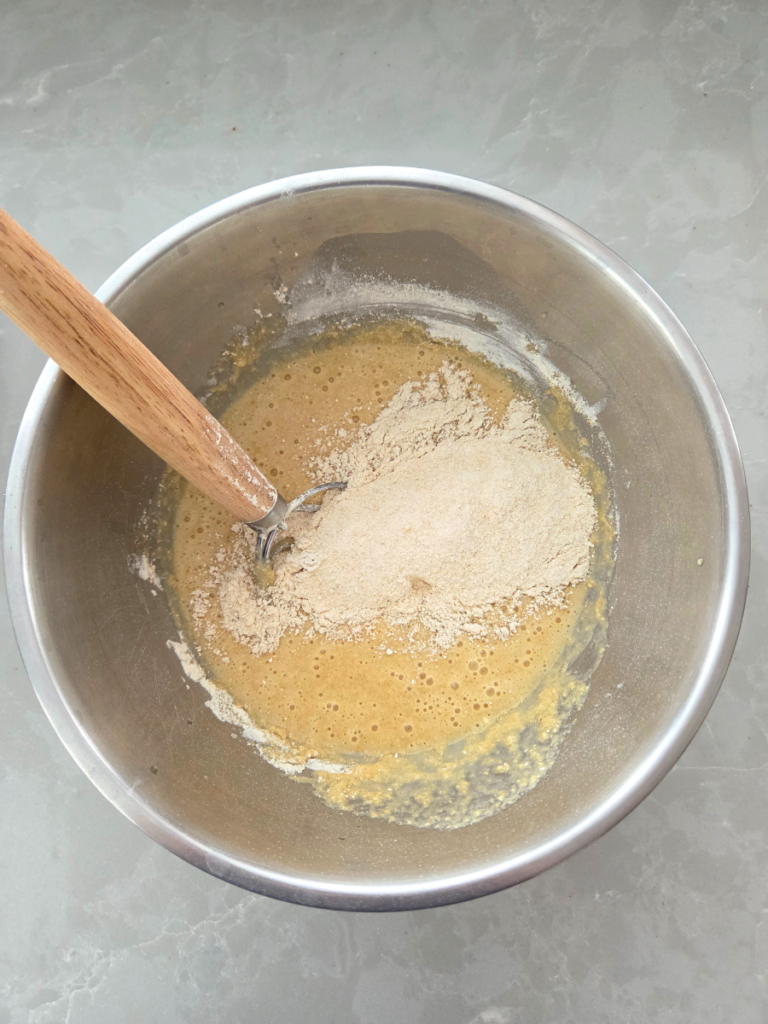 Wet ingredients being stirred into fresh milled flour muffin batter in a mixing bowl.