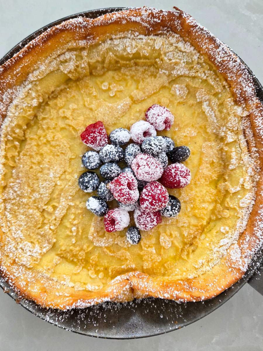 Fresh milled flour Dutch baby pancake baked in a cast iron skillet with powdered sugar and berries