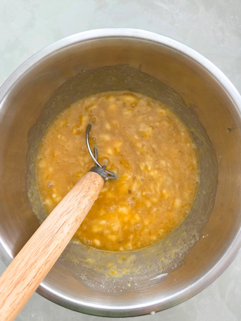 Mashed bananas being mixed into wet ingredients for banana bread.