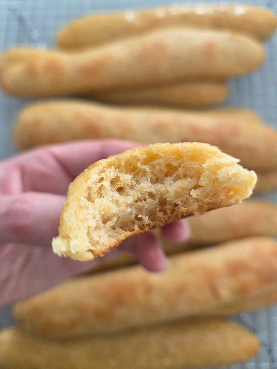 Soft and fluffy fresh milled flour breadstick showing airy interior crumb, held by hand with baked breadsticks in background.