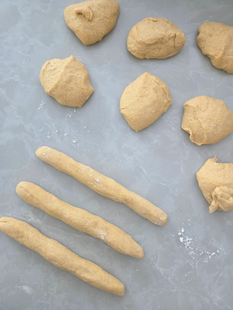 Fresh milled breadstick dough divided into portions and rolled into long ropes on a lightly floured surface.
