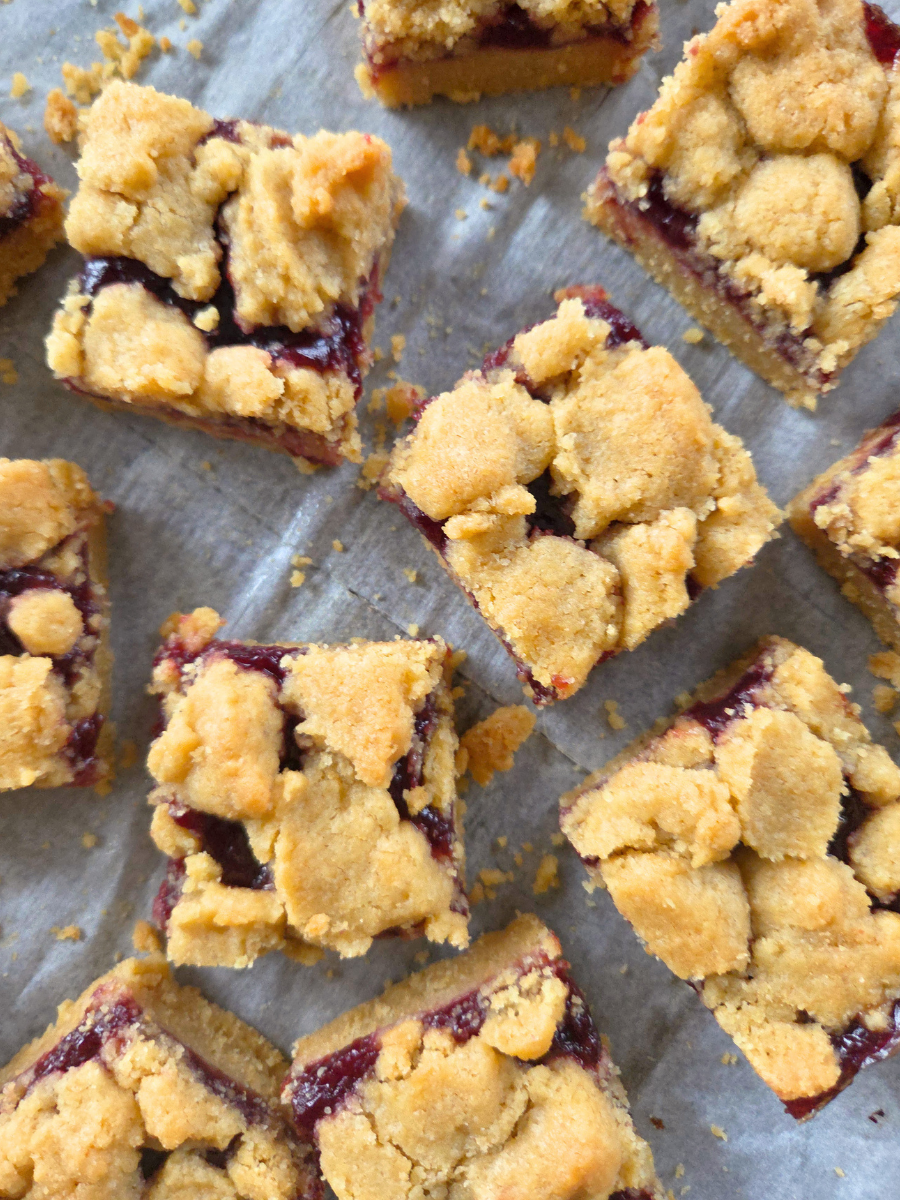 Fresh milled flour jam bars cut into squares with buttery crumble topping and berry jam filling on parchment paper.