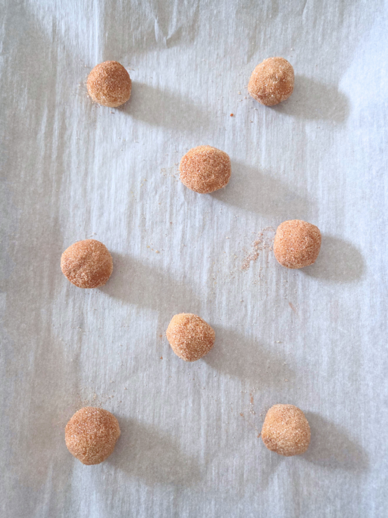 Cinnamon sugar coated snickerdoodle cookie dough balls arranged on parchment paper before baking.