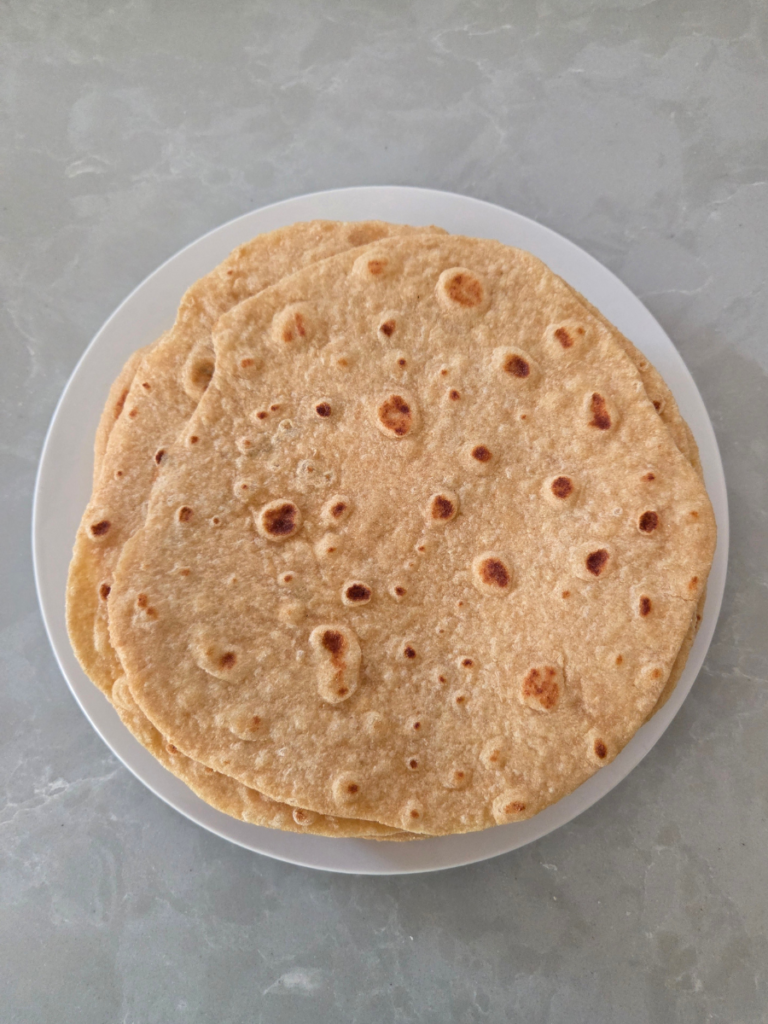 Stack of homemade fresh milled flour tortillas on a white plate with light golden brown spots.
