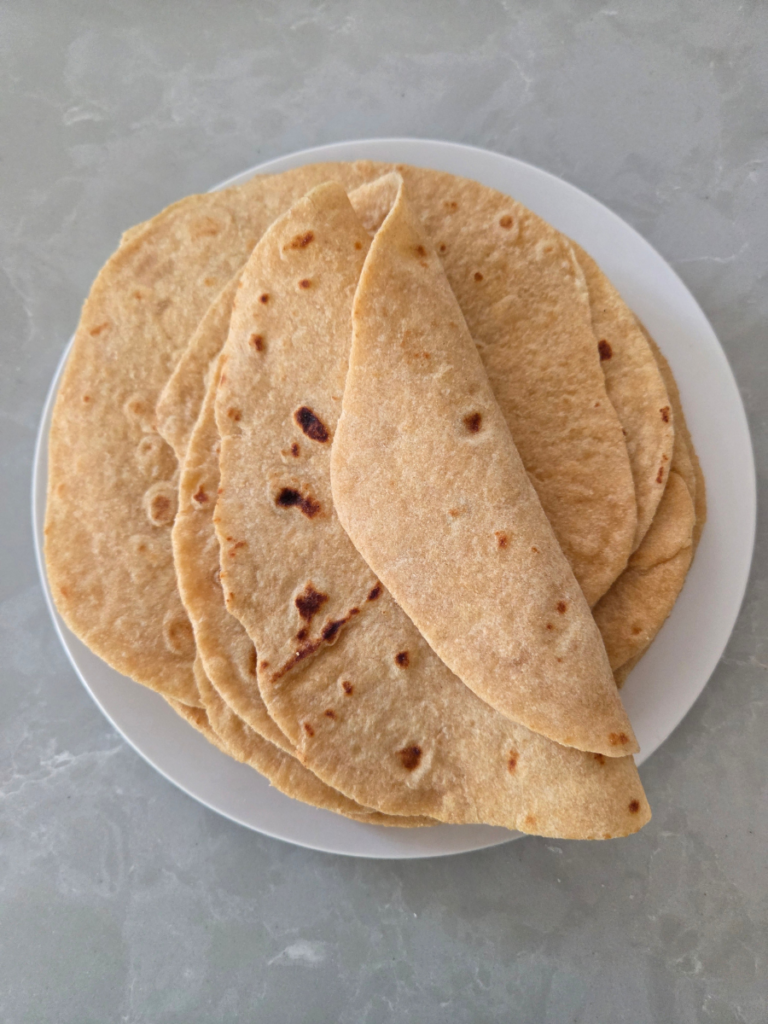 Soft homemade freshly milled tortillas folded in half and stacked on a plate.