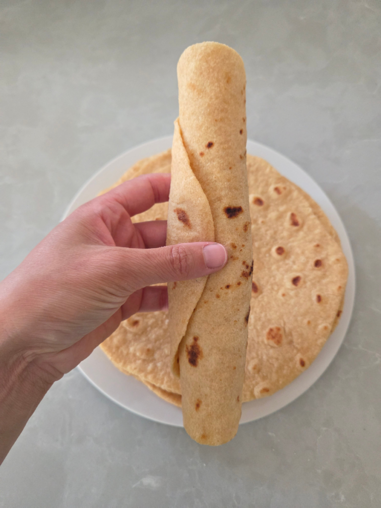 Hand holding a fresh milled rolled tortilla to show its flexibility and soft texture.