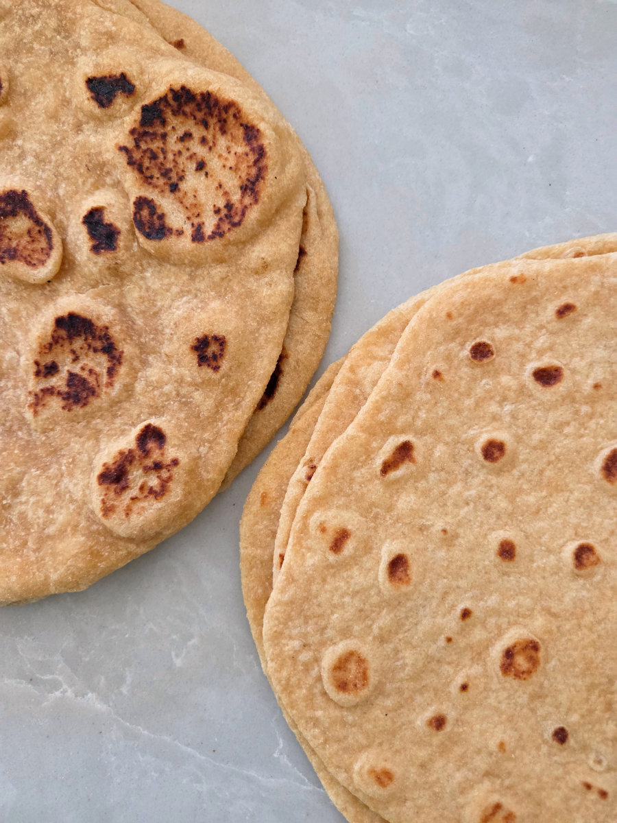 Fresh milled flour flatbread and tortillas cooked until golden brown and served warm on a light gray plate.