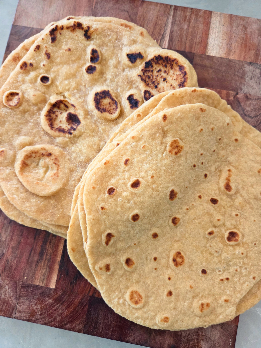 Stack of homemade fresh milled flour tortillas and flatbread with golden brown spots, showing their soft and pliable texture.