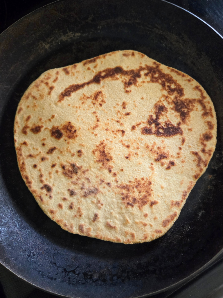 Golden brown flatbread with charred spots after cooking in a cast iron skillet.
