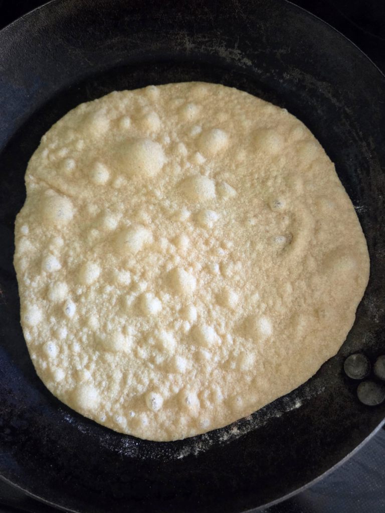 Homemade tortilla cooking in a hot skillet with small bubbles forming before flipping.