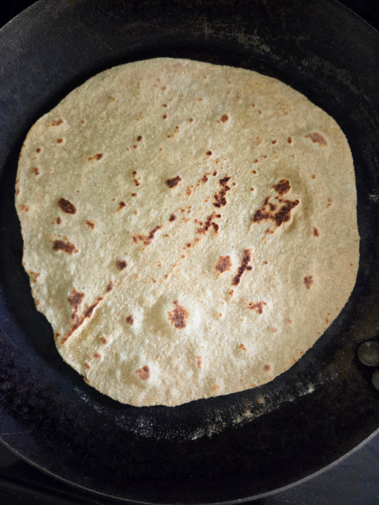Soft tortilla with light golden brown spots cooking in a dry skillet.