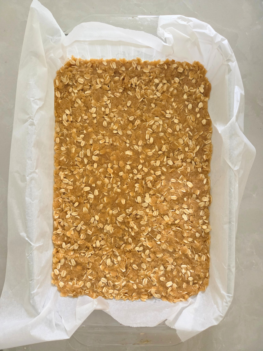 Fresh milled flour oat crumble mixture pressed into a parchment-lined baking pan to form the crust.
