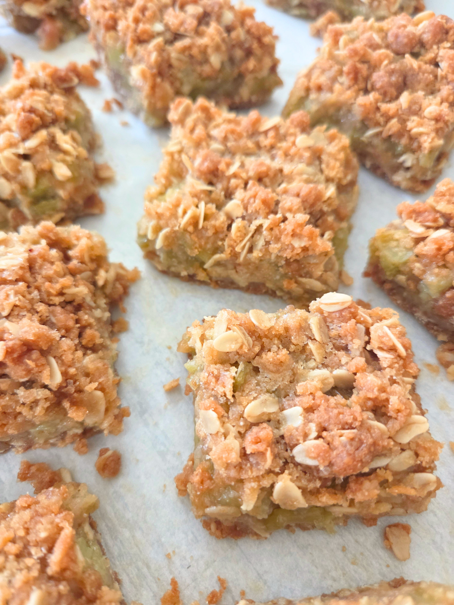 Freshly Milled Rhubarb Crumble Bars on parchment paper with golden oat crumble and sweet-tart rhubarb filling.
