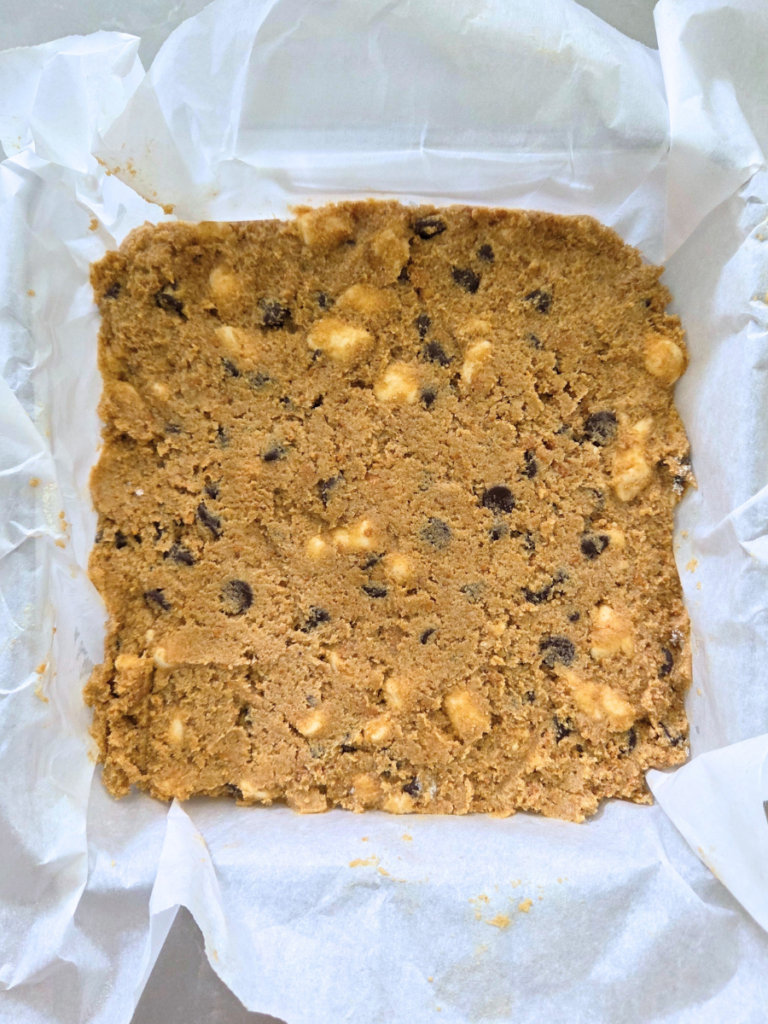 S'mores cookie bar dough pressed into a parchment lined baking pan before baking.