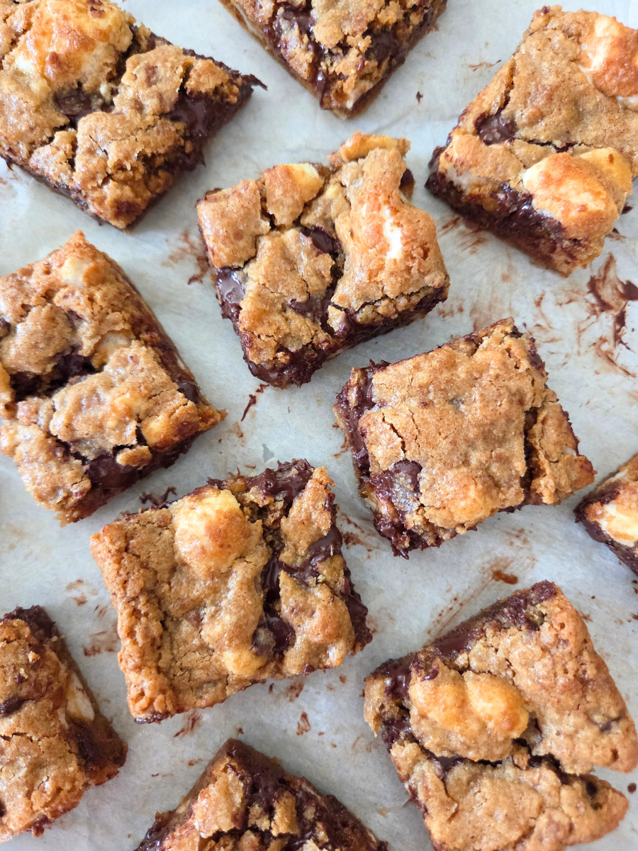 Fresh milled flour s'mores bars with golden chewy tops, melted chocolate, and gooey marshmallows on parchment paper.