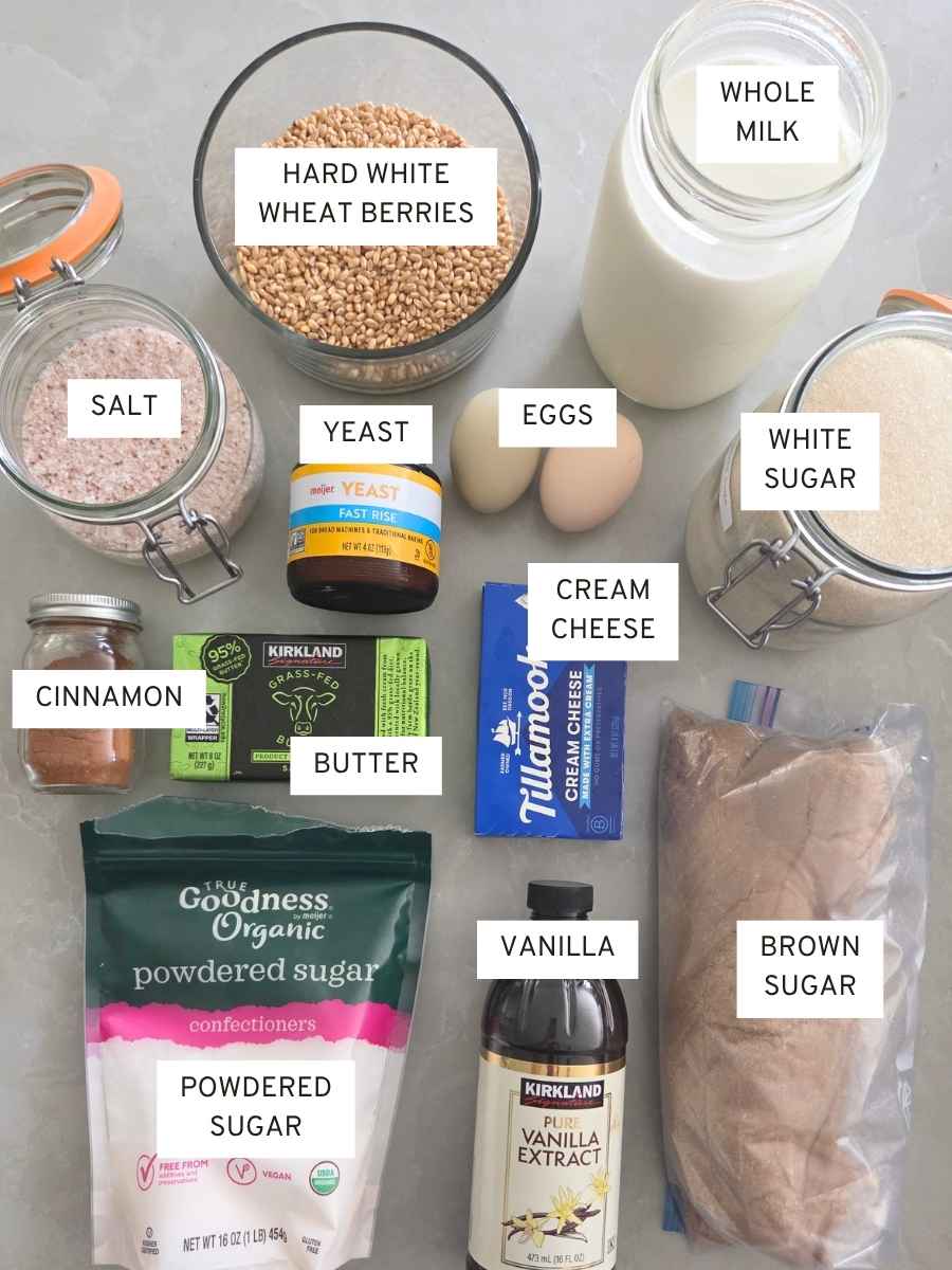 Ingredients for fresh milled flour cinnamon rolls, including hard white wheat berries, milk, butter, eggs, yeast, cinnamon, sugars, vanilla, and cream cheese.