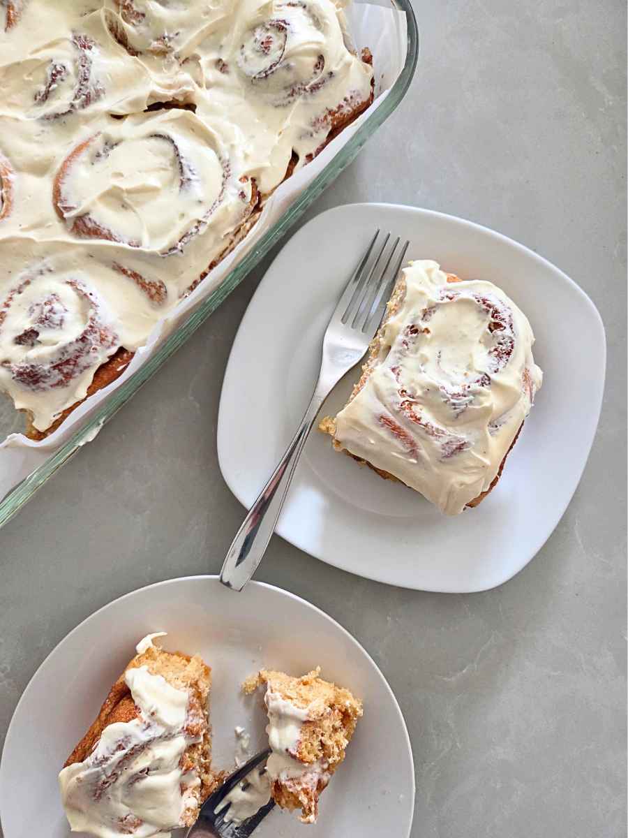 Fresh milled flour cinnamon rolls with cream cheese frosting served on plates beside the baking dish.