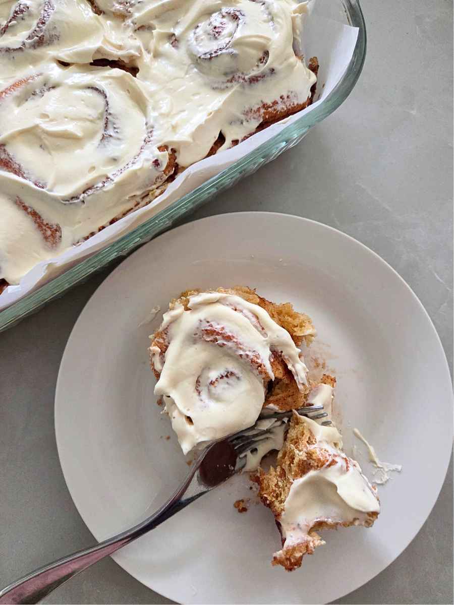 Fresh milled flour cinnamon roll with cream cheese frosting served on a plate beside the baking dish.