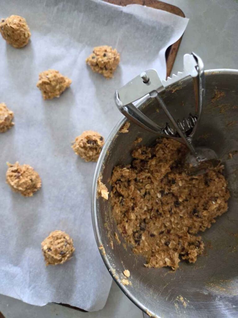 Scooping cowboy cookie dough onto a parchment lined baking sheet