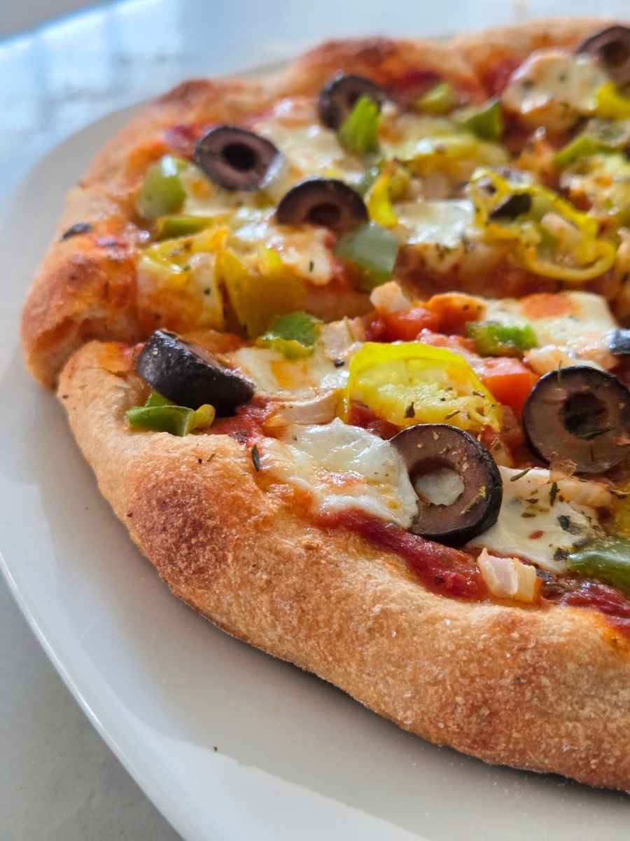Fresh milled flour pizza dough recipe topped with mozzarella, olives, peppers, and vegetables