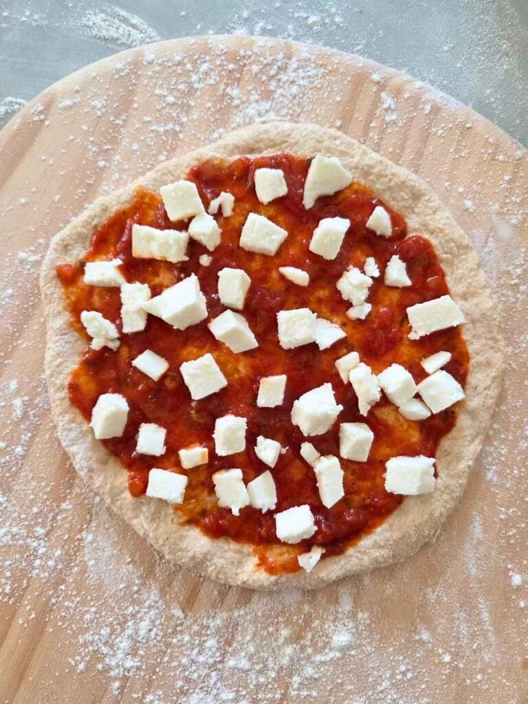 Fresh milled flour pizza dough topped with tomato sauce and fresh mozzarella before baking