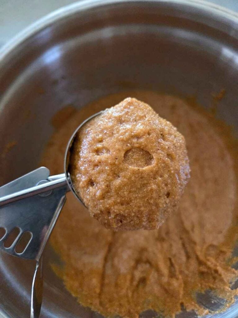 Pumpkin muffin batter being portioned with a cookie scoop.
