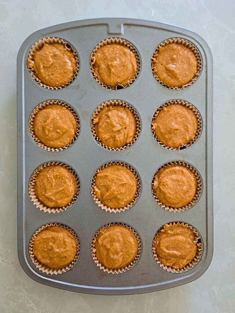 Muffin cups filled with pumpkin batter and ready for the oven.