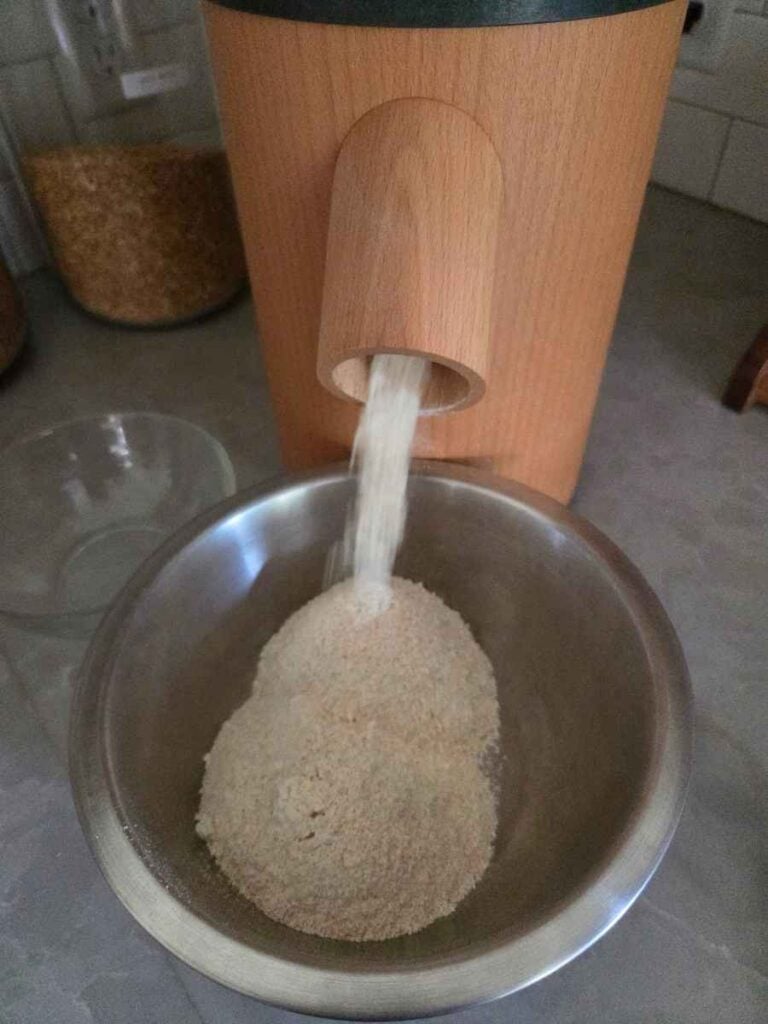 Soft white wheat berries being ground in grain mill and added to a mixing bowl.
