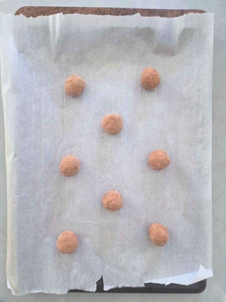 Cinnamon sugar-coated cookie dough balls spaced apart on a parchment-lined baking sheet.