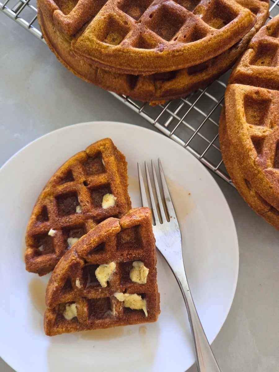 Fresh milled flour pumpkin waffles with butter and maple syrup, with more waffles cooling on a wire rack