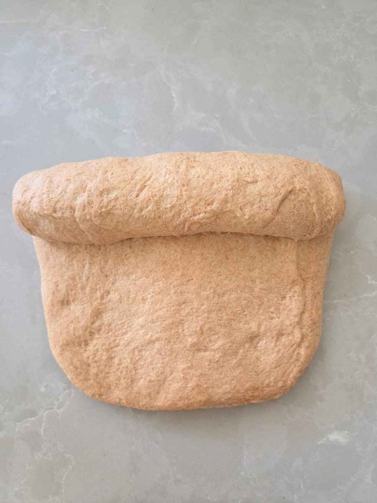 Bread dough being tightly rolled from one short end to form a sandwich loaf before placing it in the pan.