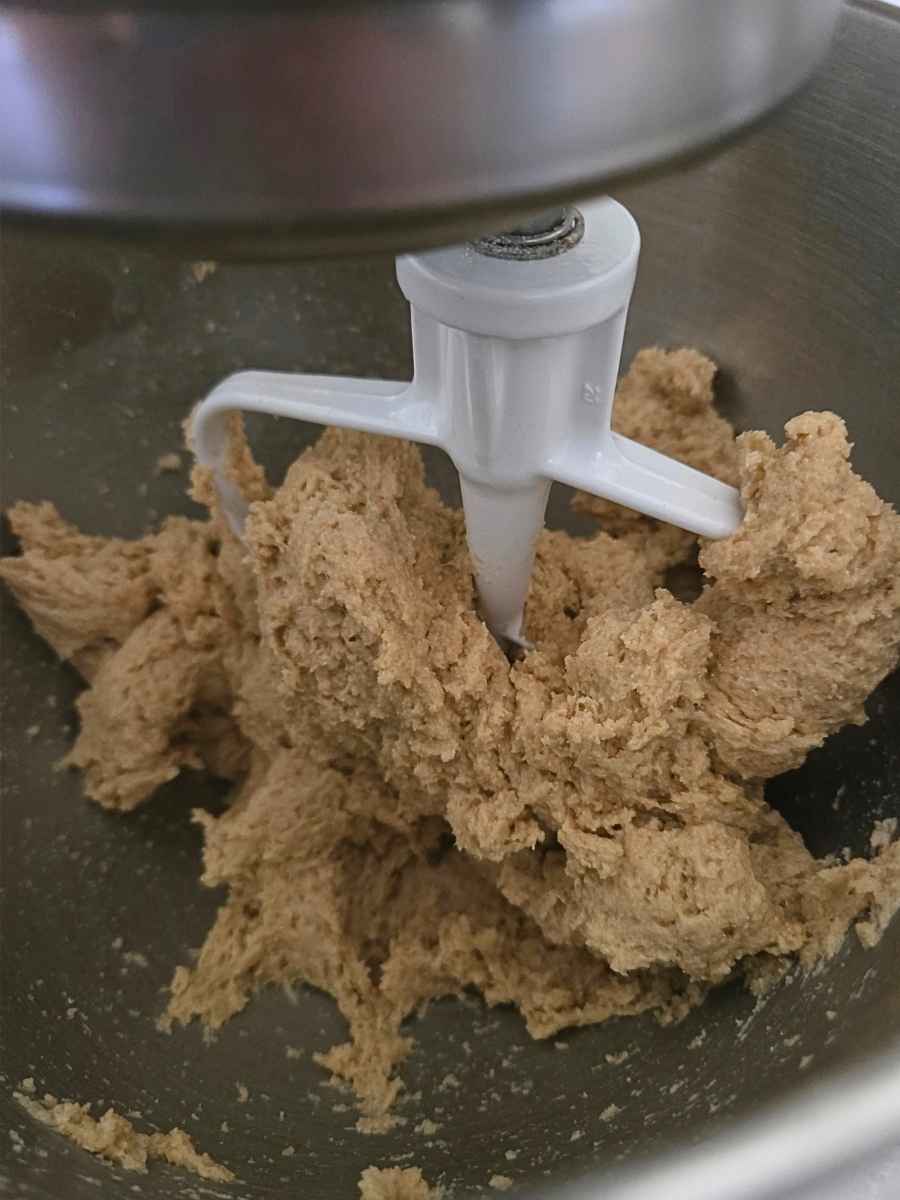 Whole wheat bread dough being mixed with a paddle attachment in a stand mixer.