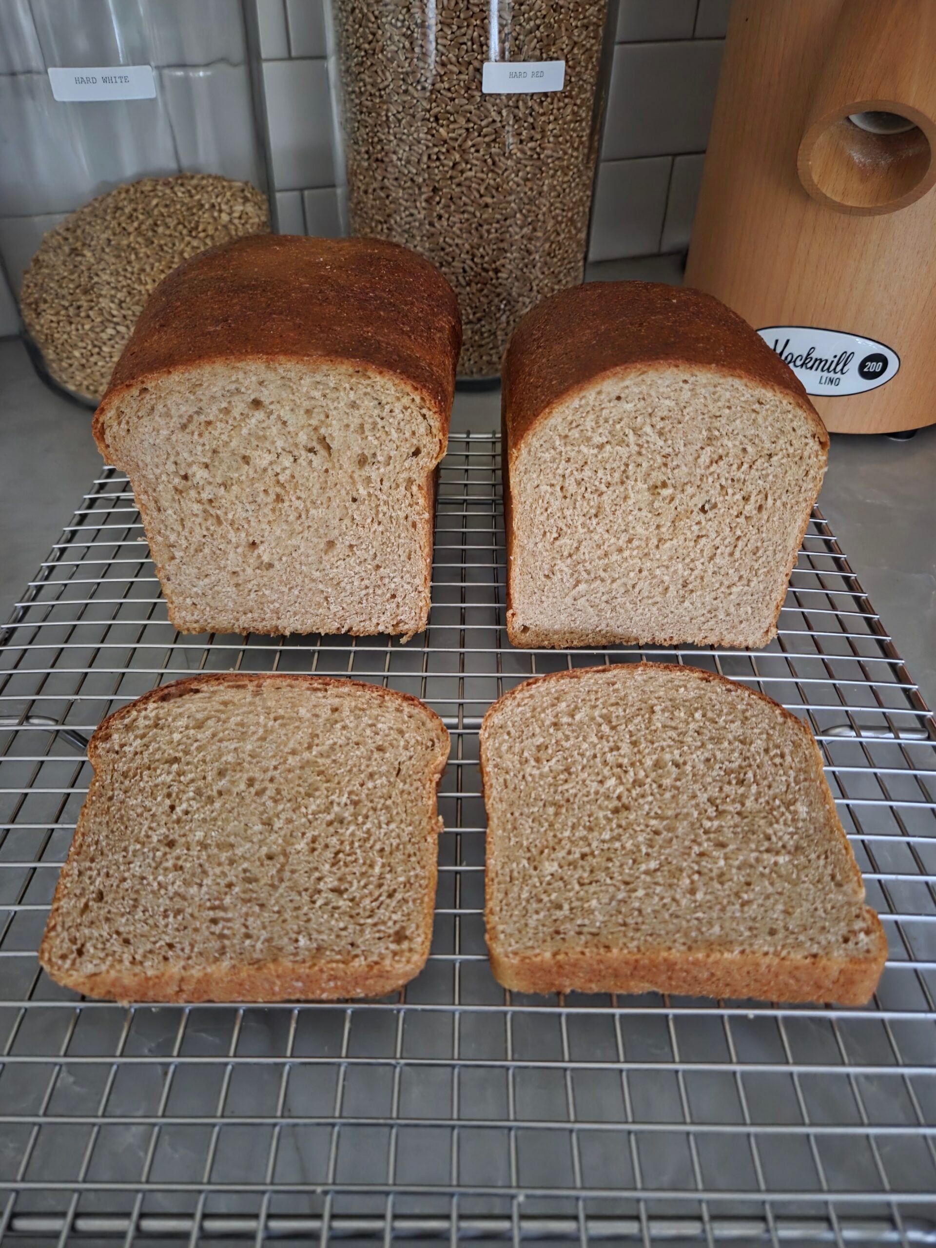 Two sliced loaves made with this fresh milled flour sandwich bread recipe, showing their soft, fluffy crumb and golden brown crust on a wire cooling rack.