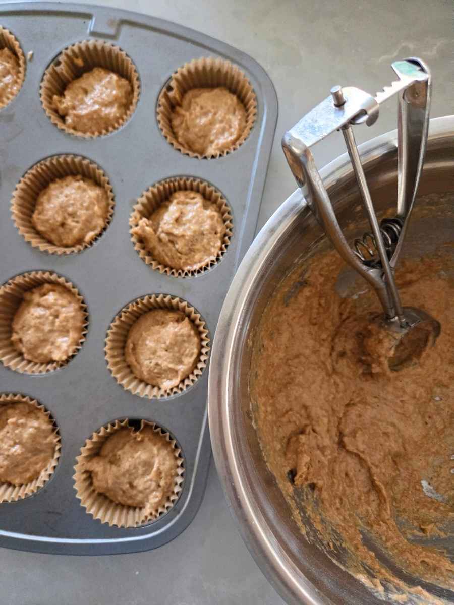 Spoonfuls of muffin batter being added to a lined muffin pan