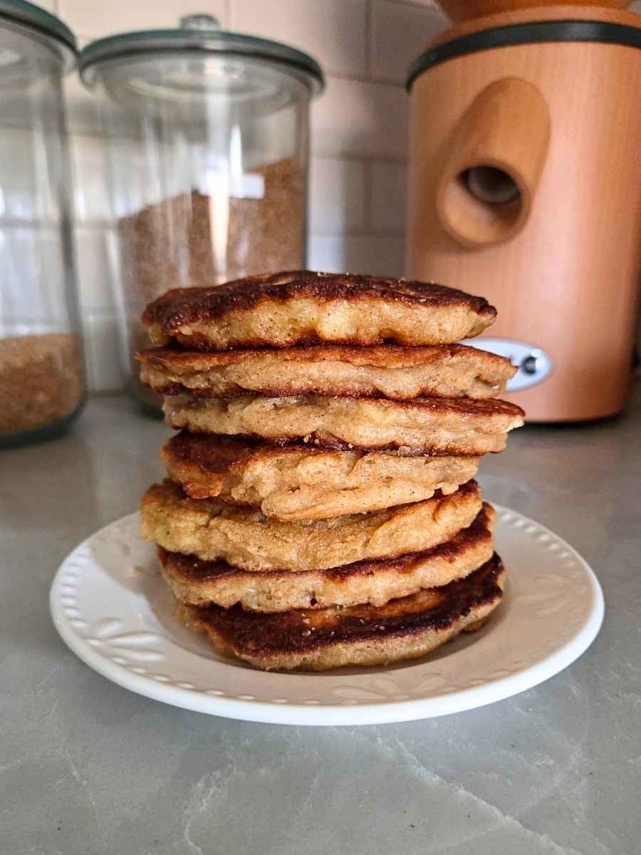Tall stack of homemade fresh milled flour apple fritter pancakes showing their fluffy centers and golden, crispy edges.