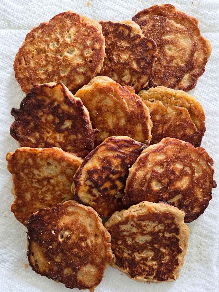 Homemade apple pancakes with golden brown, crispy surfaces cooling on a paper towel.