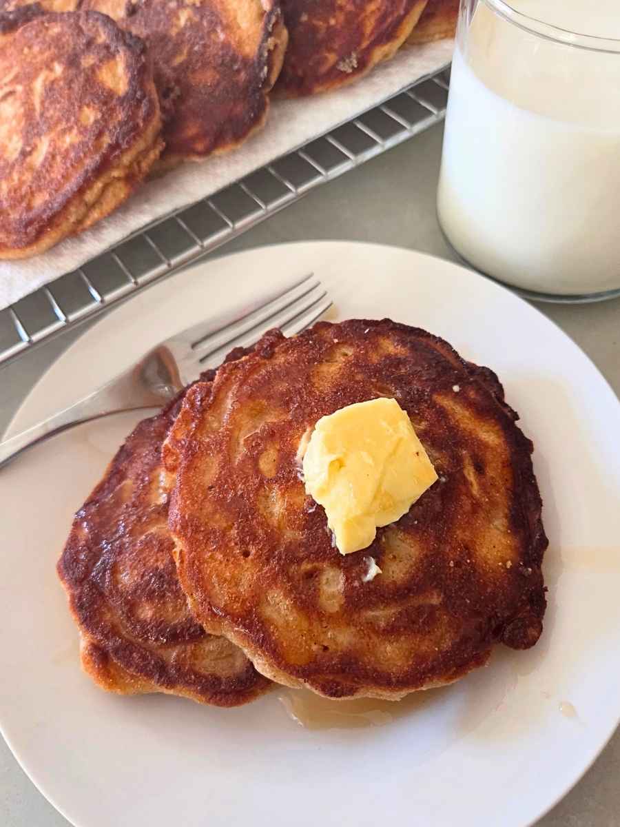 Two fresh milled flour apple fritter pancakes served with butter and maple syrup on a white plate.